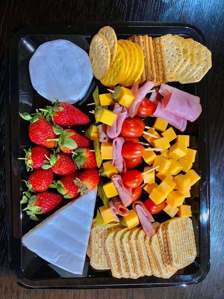 Cheese platter with brie, cheddar cubes, ham, cherry tomatoes, strawberries and crackers