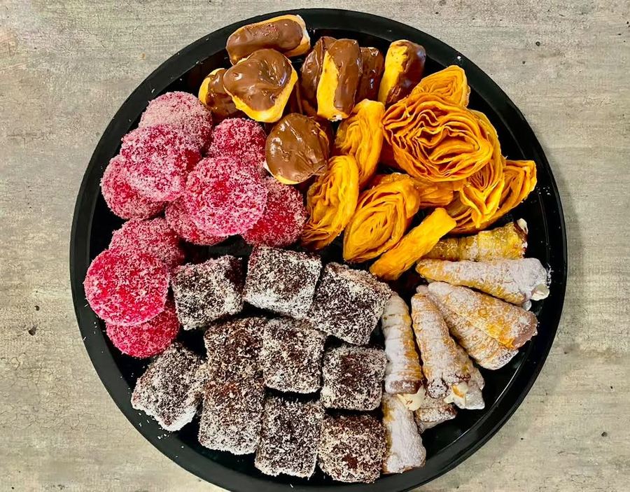 Platter of sweet fancies with chocolate éclairs, pink coconut balls, lamingtons, cream horns and pastry roses